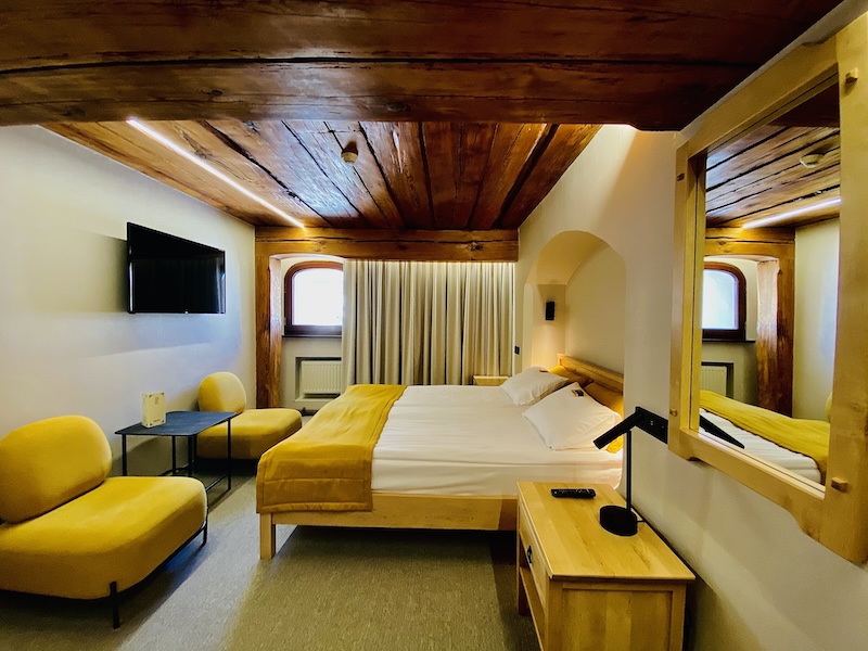 Hotel room with wooden ceiling, bed and yellow armchairs
