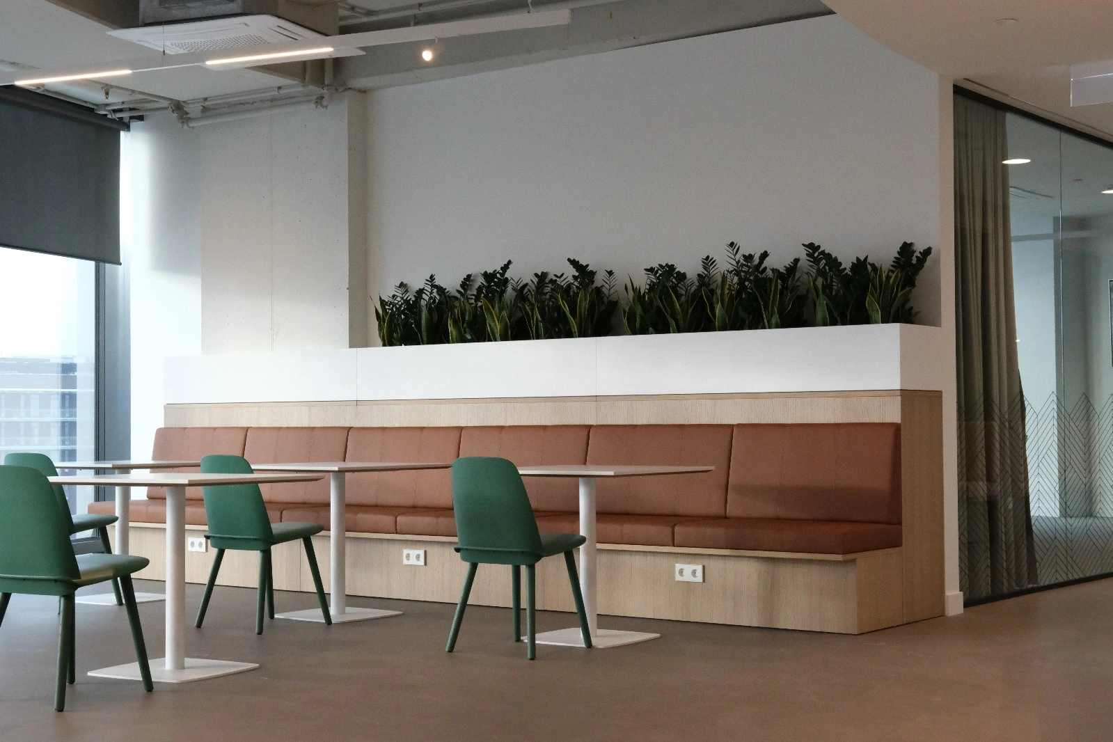 Café seating with green chairs and an upholstered bench with planters